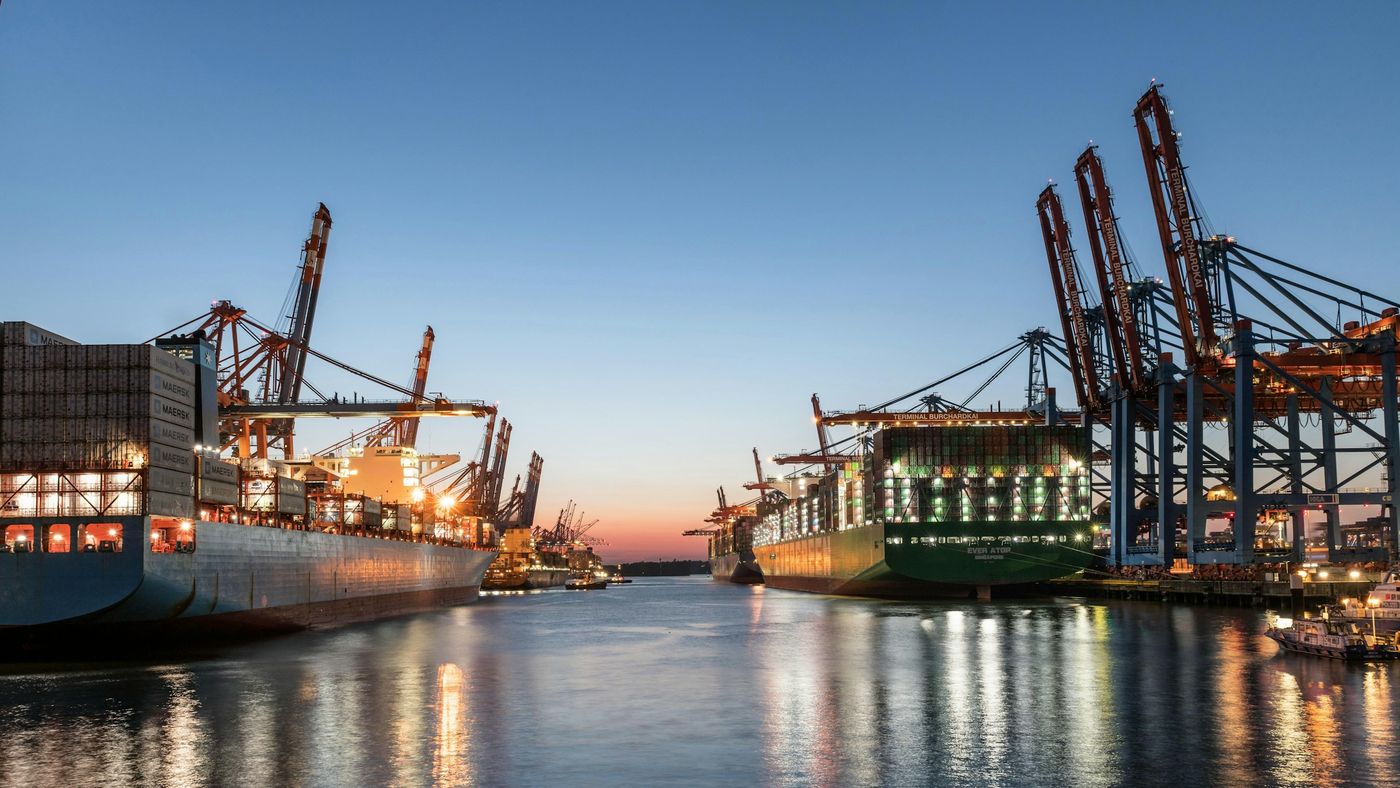 Container ships under gantry cranes at a port at dusk